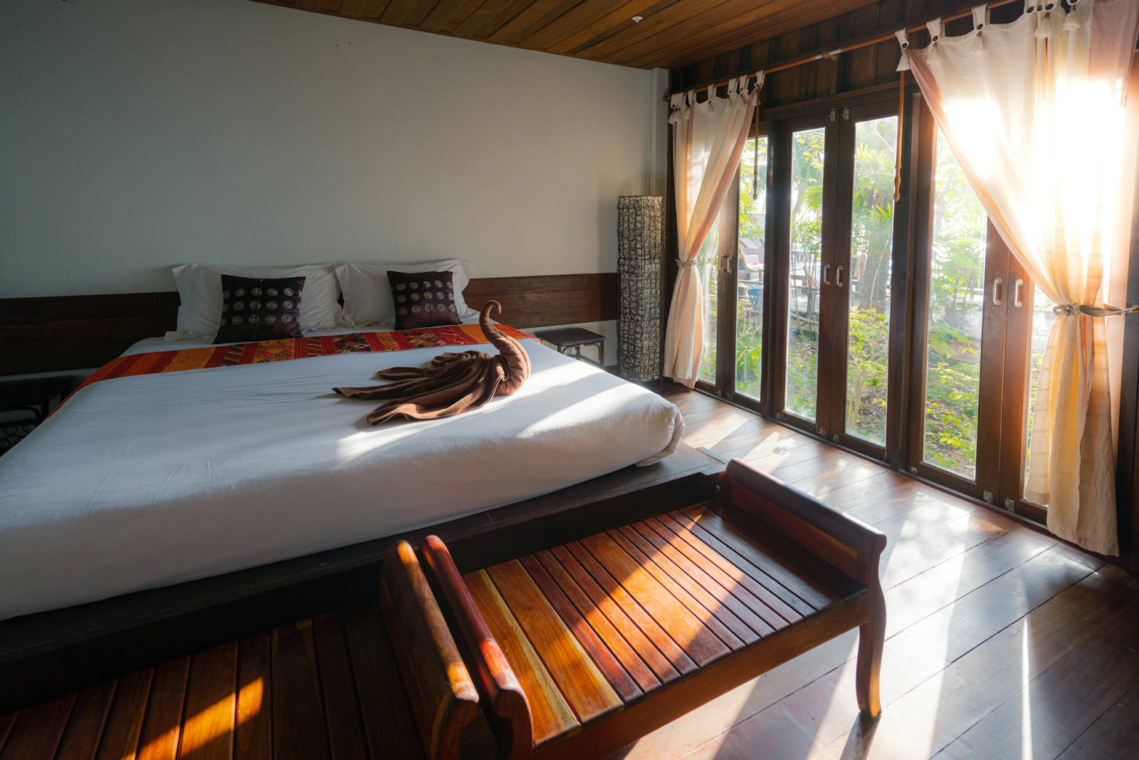 Sunlit bedroom with patterned runner, pillows, and white bedding