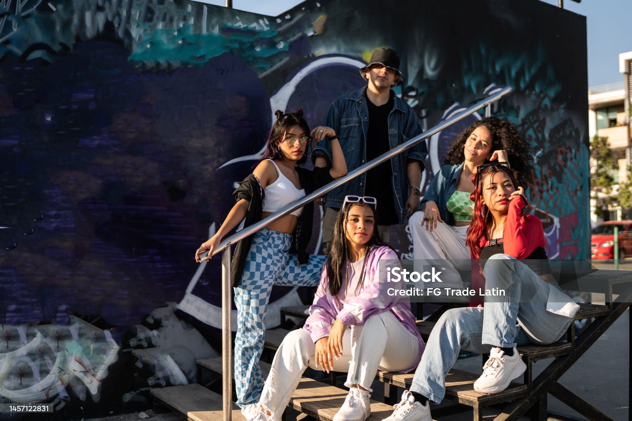Group of models in urban streetwear posing on stairs by a graffiti wall